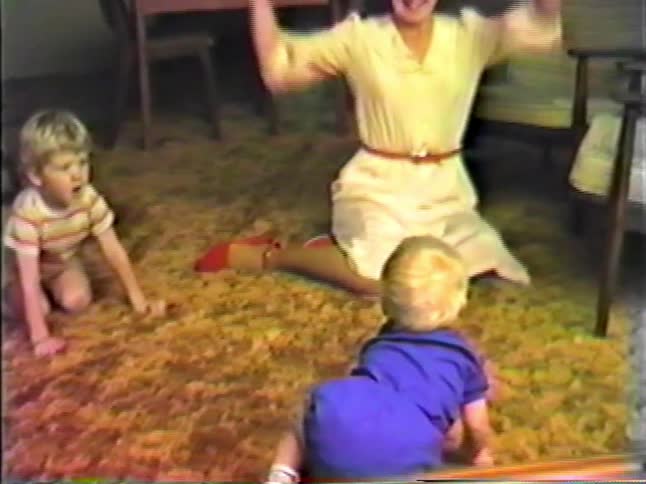 A happy mother and father play excitedly with their kids on the carpeted living room floor