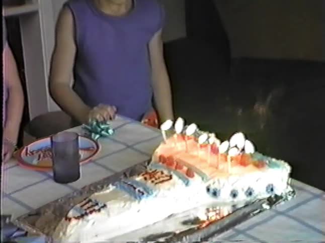 Young male boy wearing a goofy handmade headgear blowing candles over a cake in a living room indoors during day time