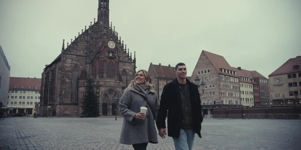 Man and woman walk on a neighborhood park street holding hands as she carries a drink