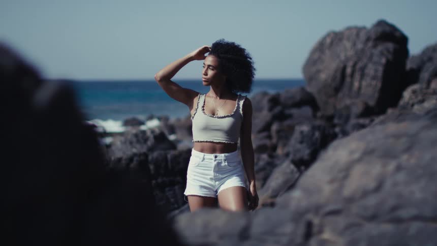 Woman standing on rocks along the coast as the wind blows her hair