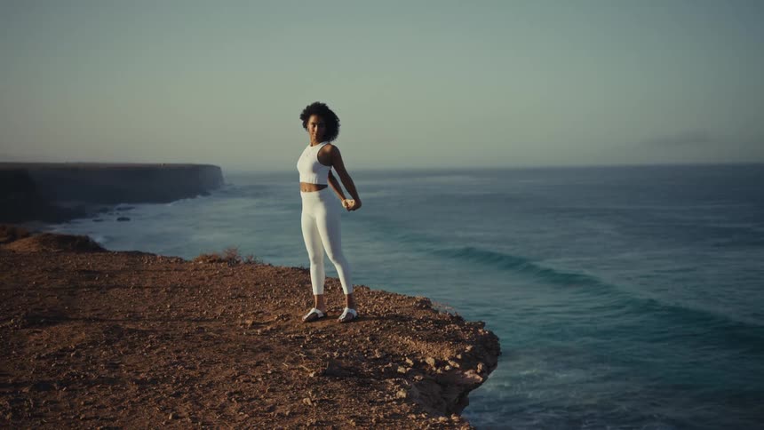 Woman standing on a ledge overlooking the coast as she exercises
