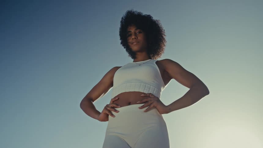 Woman stands outdoors with hands on hips under an open sky