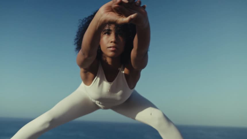 A young woman performs stretching exercises on a mat on an ocean shore