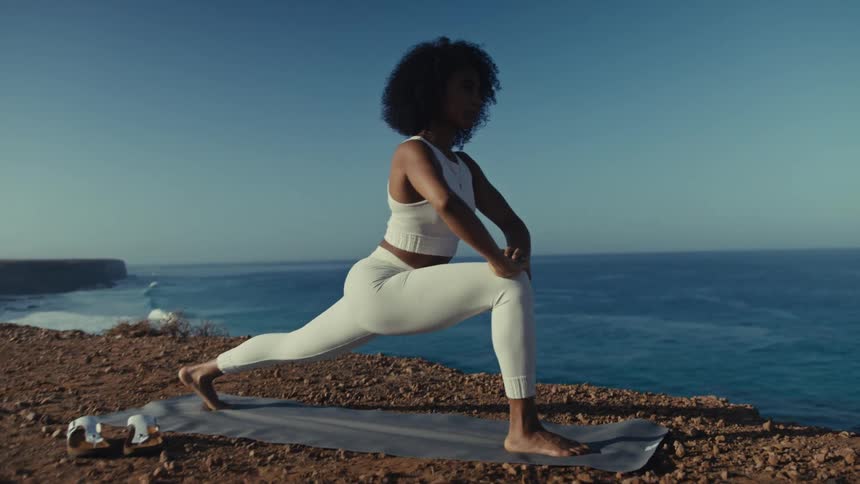 A woman flows through a graceful and powerful yoga sequence on a sundrenched cliff her strong poses silhouetted against the vast blue ocean