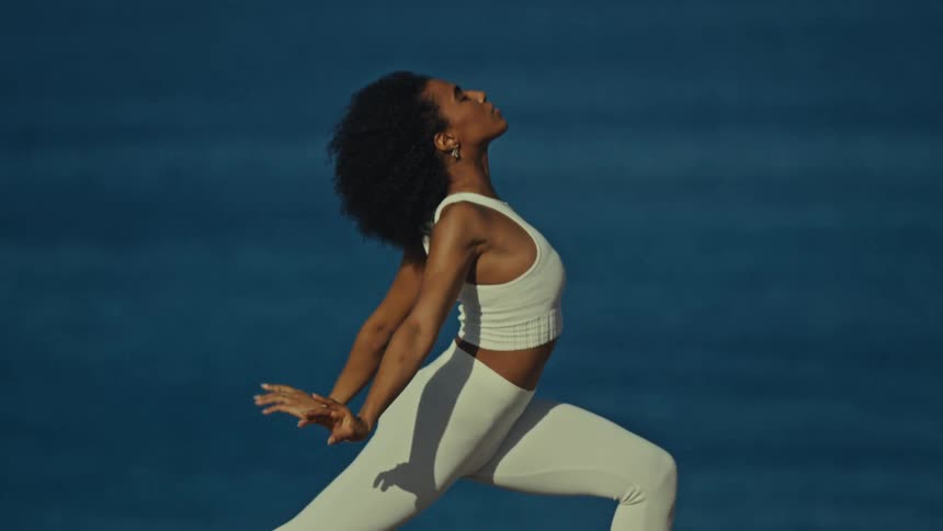 A young woman performs stretching exercises on a mat on an ocean shore