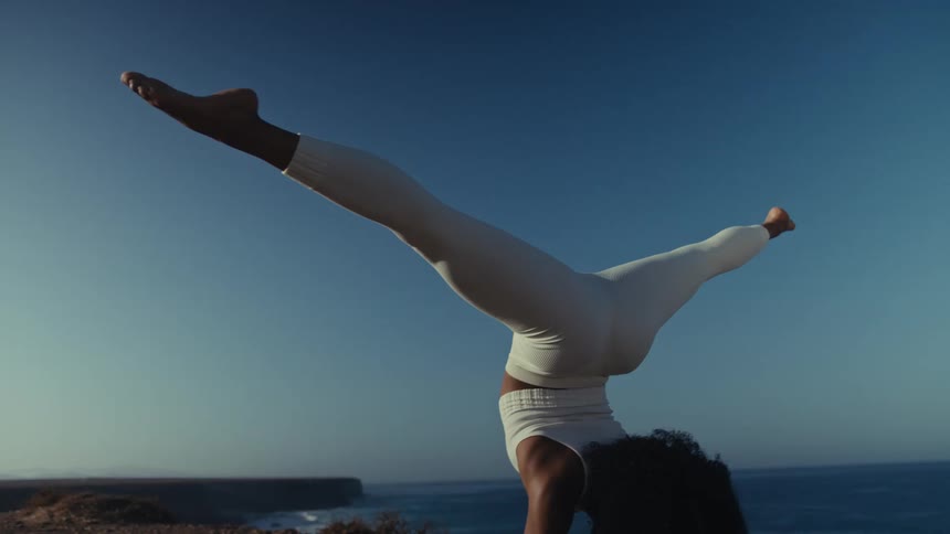 Woman performing yoga balances on her forearms while on a coastal cliff on a sunny day