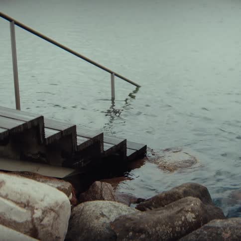 A wooden stairway leads down into a calm lake at midday surrounded by scattered rocks