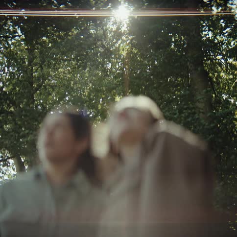 Two blurred people walking through a wooded area with sunlight filtering through the leaves