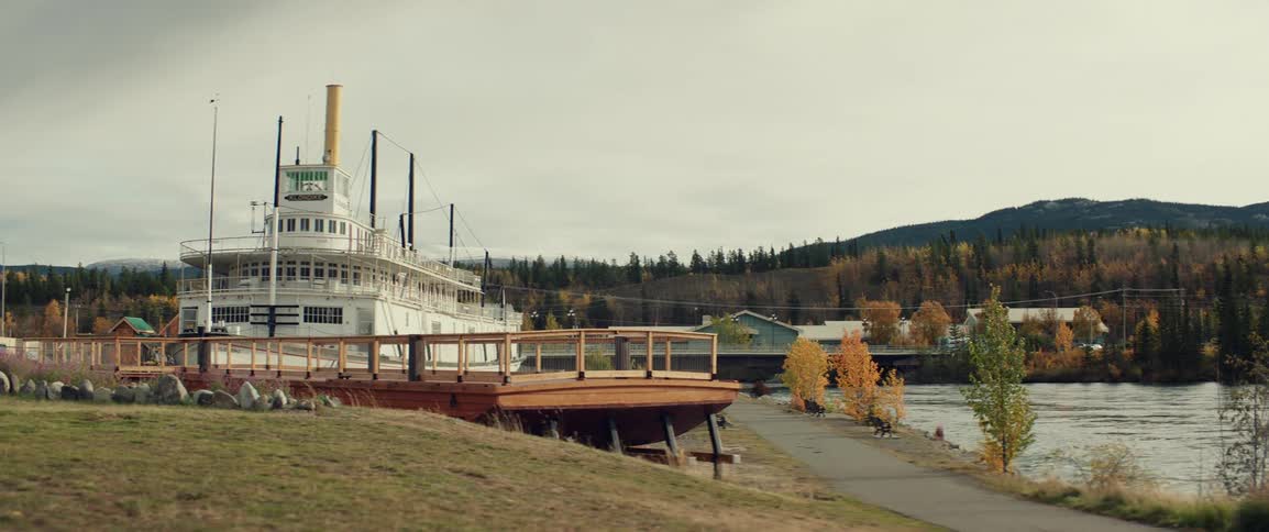 A paddlewheel boat sits beside a river under a cloudy sky