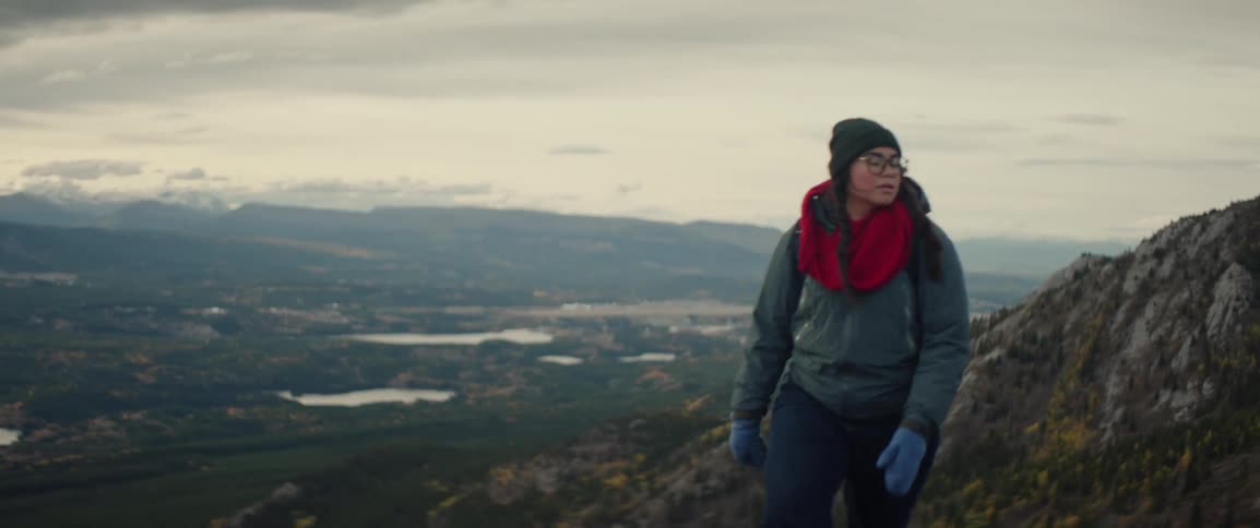A woman outdoors hiking on a mountain with a town and valley in the background