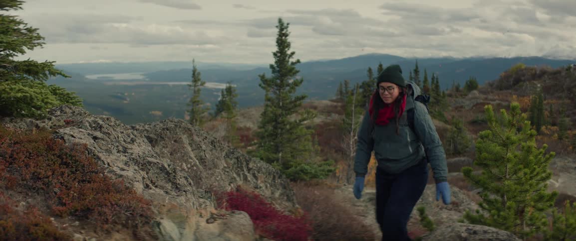 Person walking along a rocky trail in a mountainous area with autumn vegetation and surrounding trees