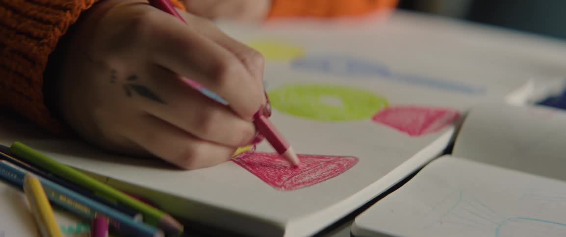Hand drawing colorful shapes with pencils in a notebook on a table