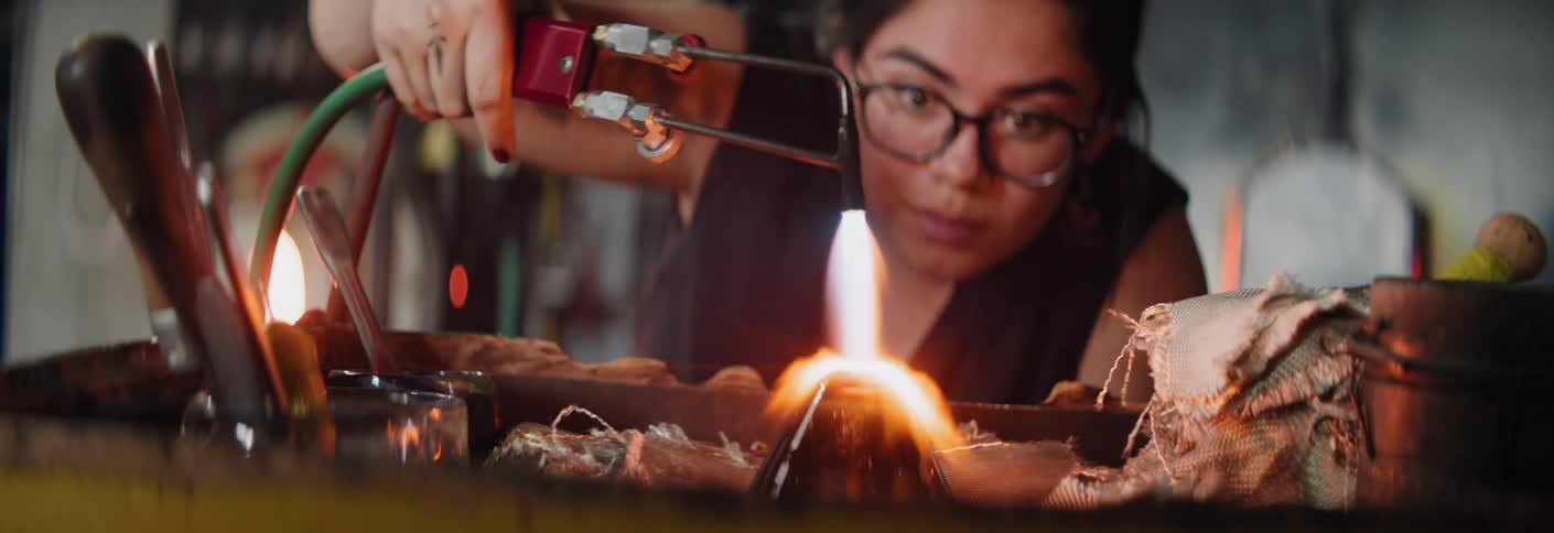 A woman working in a factory with glass uses a torch