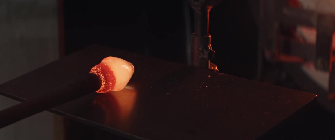 A workman shapes molten glass inside a workshop