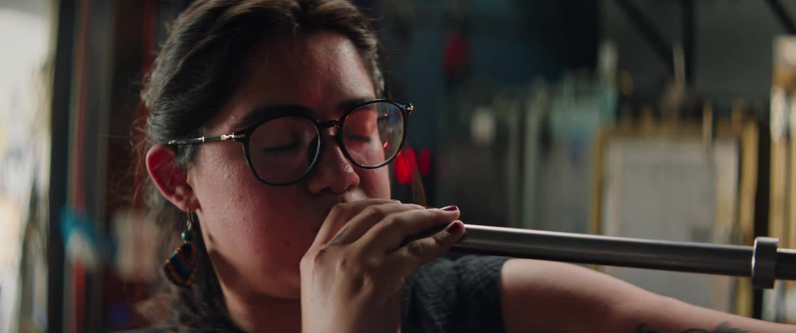 A woman blows into a glassblowing rod