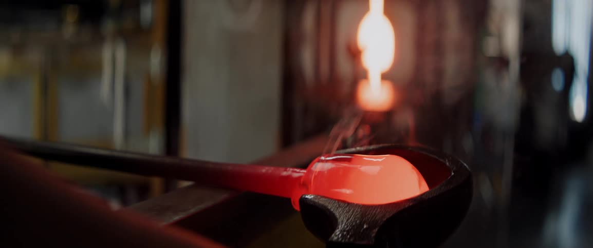 A workman shapes molten glass inside a workshop gently rolling the material to form structure