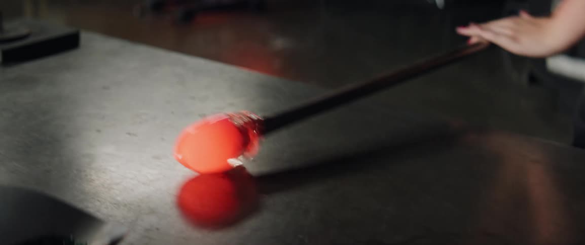 A person working molten material in a glass blowing shop