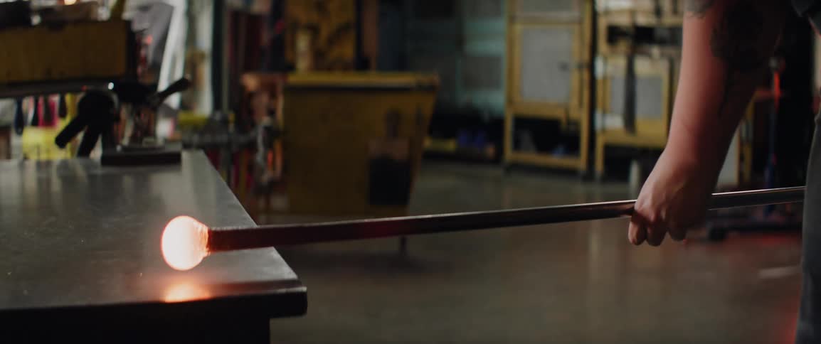 Molten glass resting on a metal rod over a worktable in a glassblowing workshop