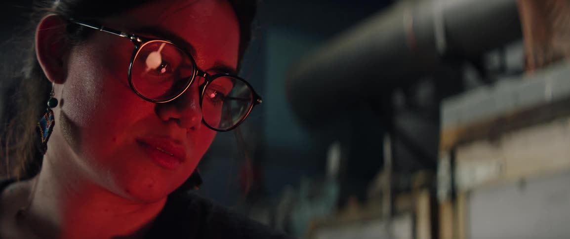 A woman with glasses focused on her craft as a hot furnace illuminates her face