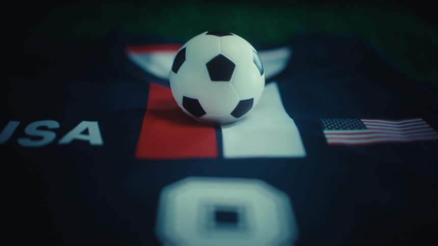 A soccer ball rests on a jersey featuring national colors and a small us flag softly lit against a dark background