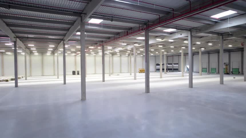 Empty industrial warehouse with polished concrete floor and metal columns under high ceiling