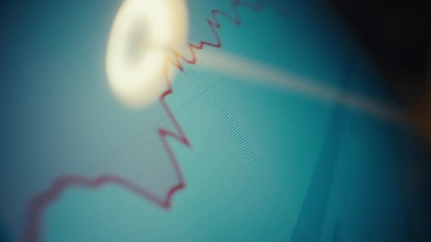 A red fluctuating line graph rises across a blue digital screen toward a glowing targetlike marker