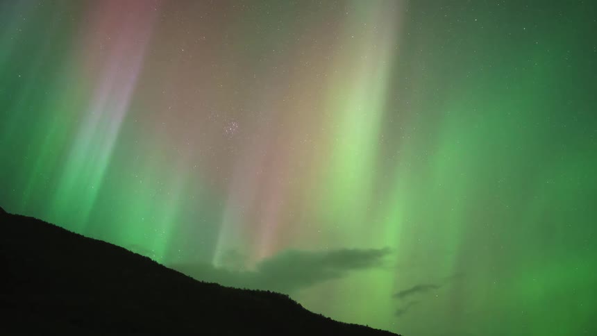 Multicolored aurora borealis rises vertically above dark mountains