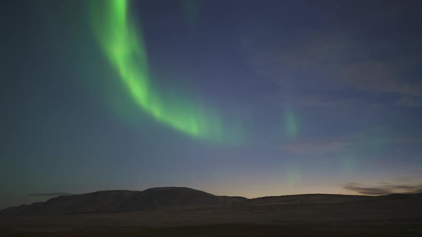 A green light hovers in the sky above a mountain range in the wilderness at sunset