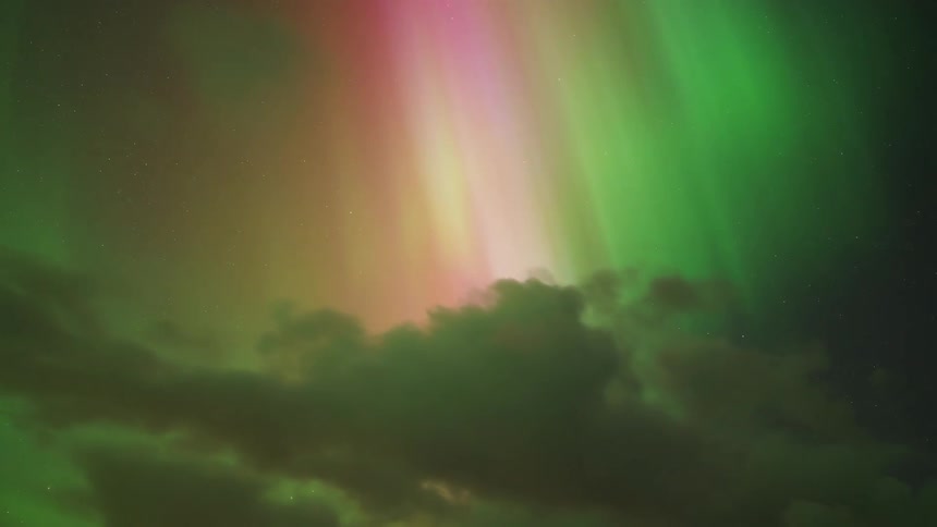 Aurora borealis with green and pink bands above illuminated clouds at night