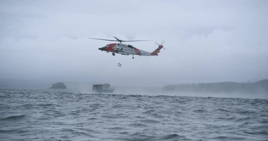 Ship sailing on rough water off the coast as a helicopter hovers in the air