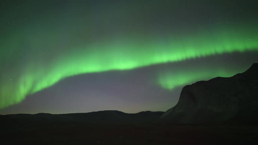 Green aurora borealis stretches over rocky mountains at dusk