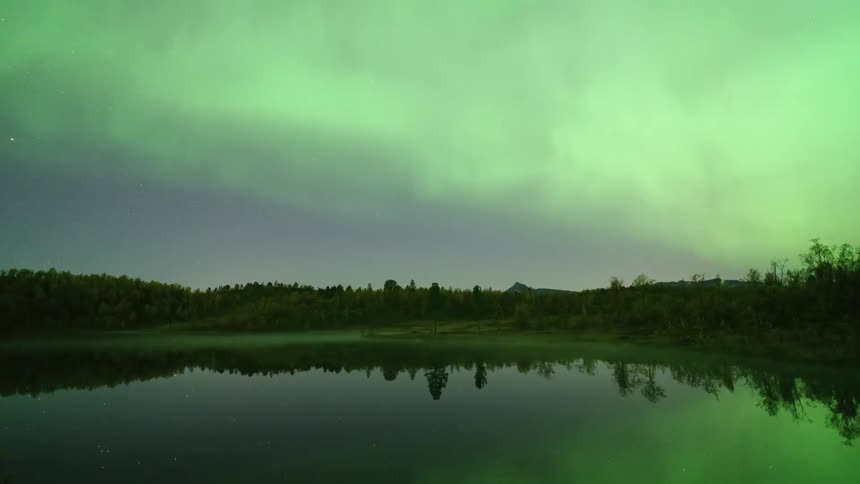 Aurora borealis reflected on a calm lake with a forested shoreline at night