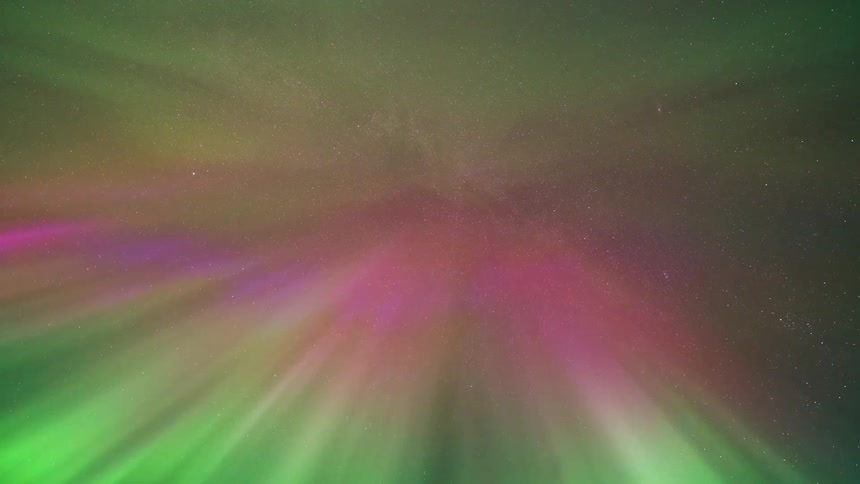 A timelapse captures vibrant green and pink northern lights swirling and dancing across a star filled night sky while the camera points directly upward toward the zenith