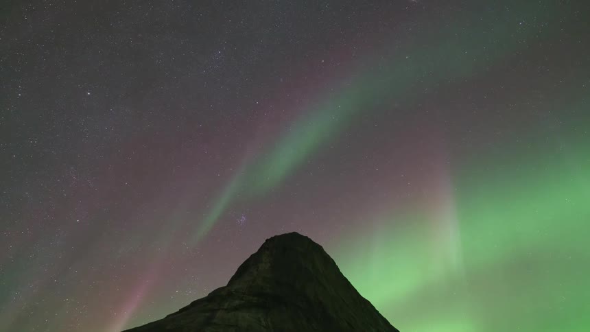 The glowing green lights of the aurora borealis glow over a mountain