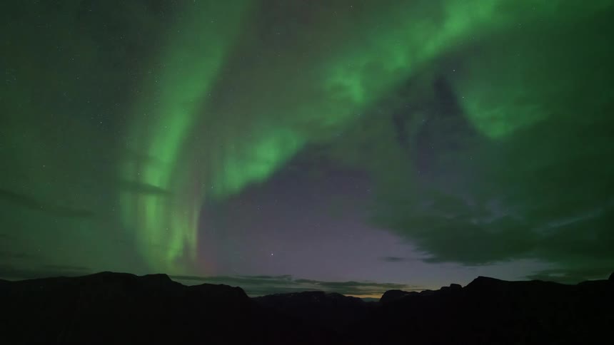Aurora borealis forming a green arc in the sky above mountainous silhouettes at night