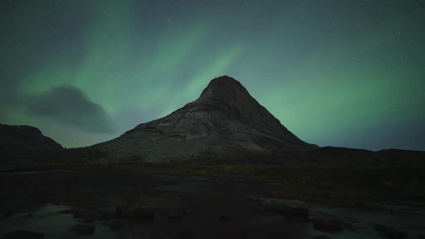 Clouds near a mountain as darkness falls and the northern lights move across the sky