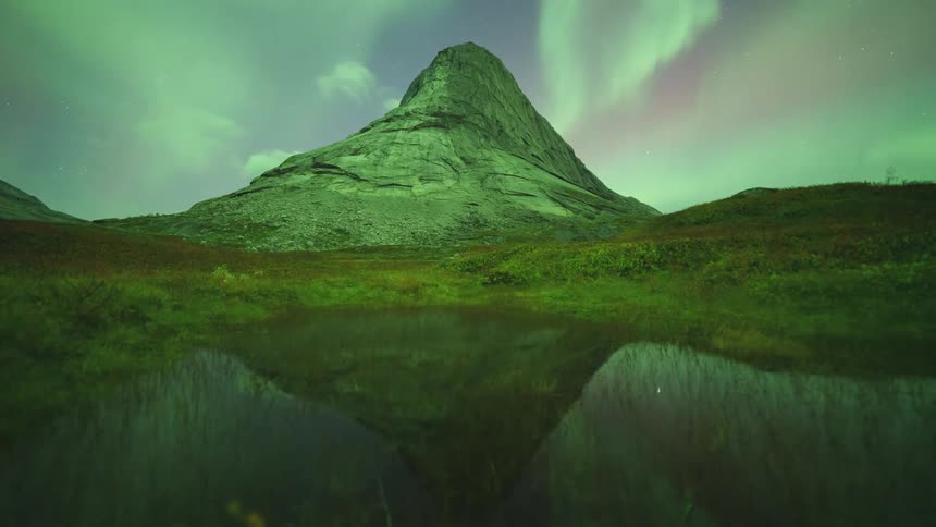 Mountains along the coast as the northern lights illuminate the night sky