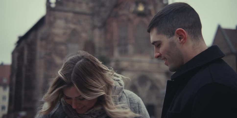 A smiling couple takes a selfie then kisses together in front of a historic building capturing a cheerful moment during their visit