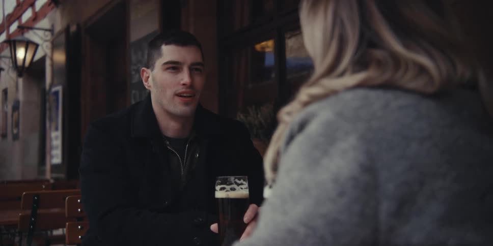 Man and woman sitting at an outside table with glasses of beer as they talk