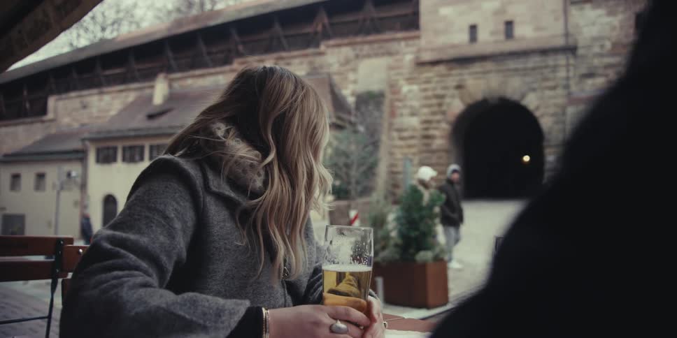 A woman sits outside at a table while having a beer with a friend
