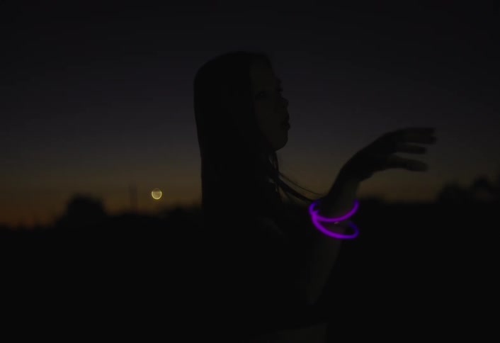 A woman performs slow expressive dance movements outdoors at night