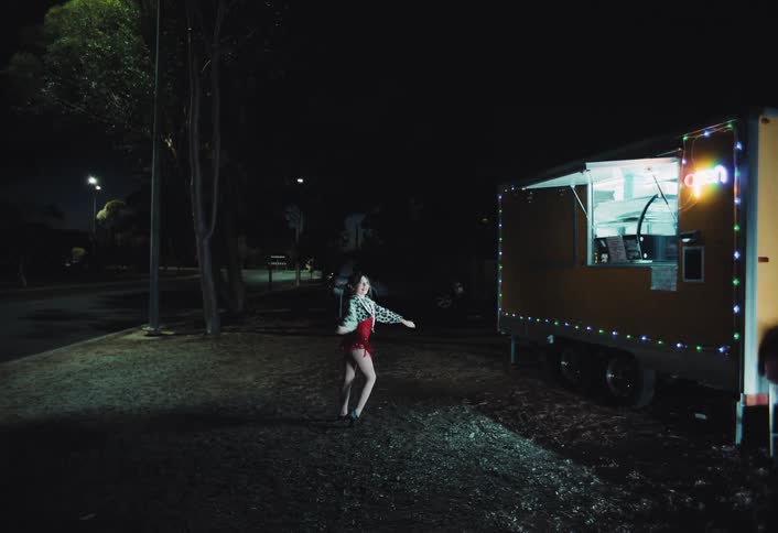 Woman dances outdoors at night beside a lit food truck