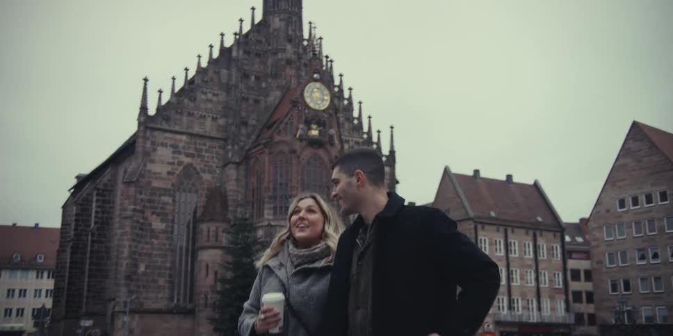 Man and woman walking together on a road outside of a cathedral as she carries a cup