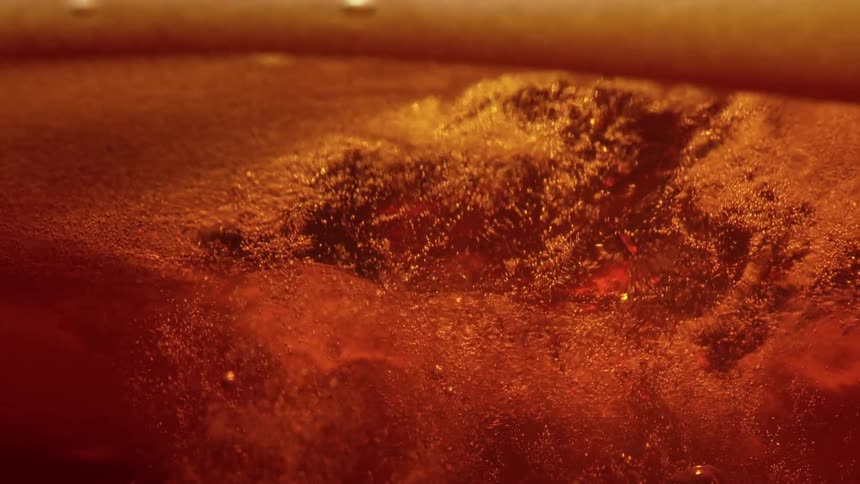 Closeup of a molten orangegolden textured liquid surface with small glowing yellow sparksand rolling twirling bubbles