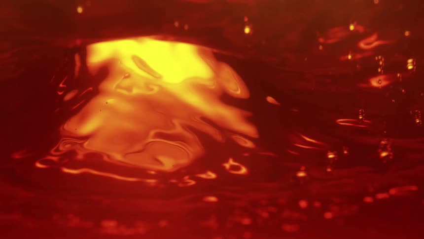 A large volume of amber liquid creates a deep whirlpool as air is pulled beneath the surface forming glowing golden bubbles and turbulent ripples that transition from bright yellow to deep crimson across the frame