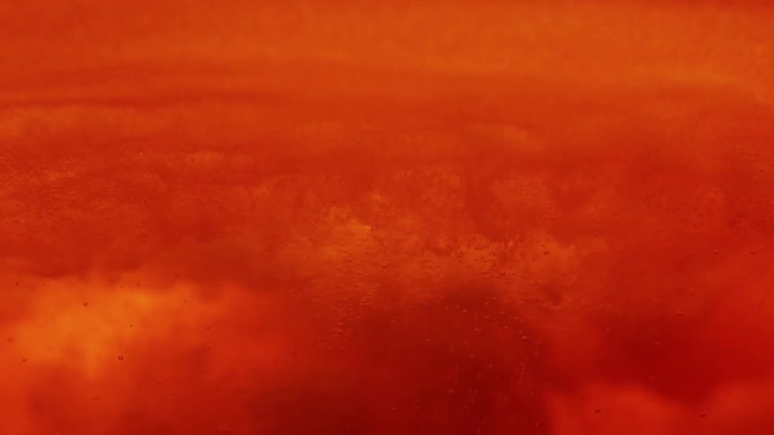 Orange liquid surface with density variations and suspended particles