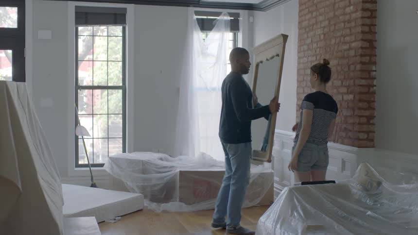 A man and woman remove a mirror from a living room wall