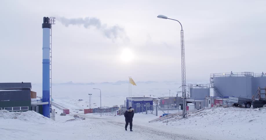 Man walking on a road by factory buildings as smoke flows from a tower chimney on a winter day