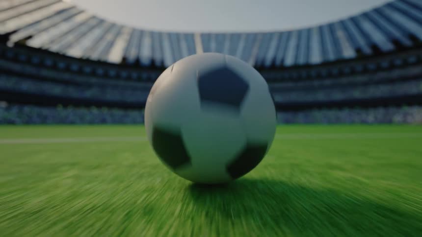Soccer ball rolling across the grass with stadium stands in the background