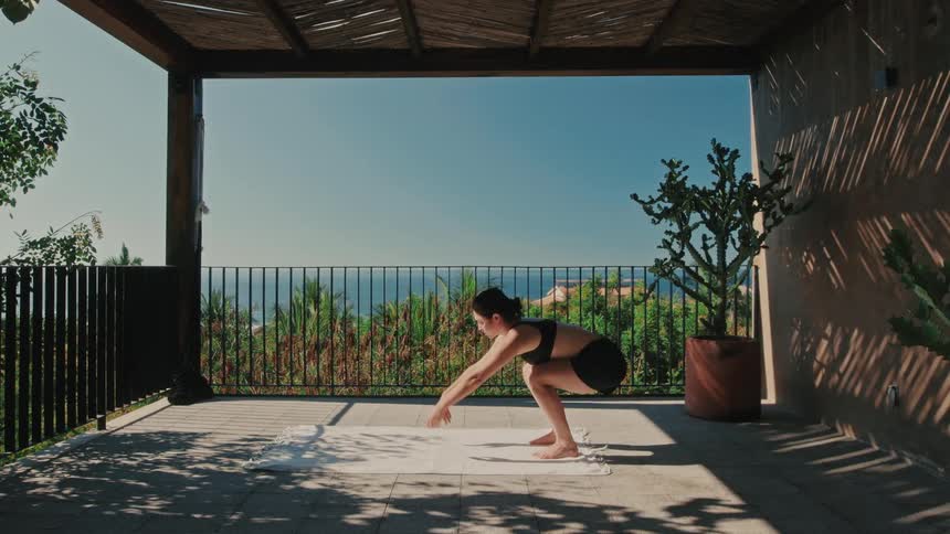 Woman moves from standing foldedover position to squatting with arms outstretched in a covered porch